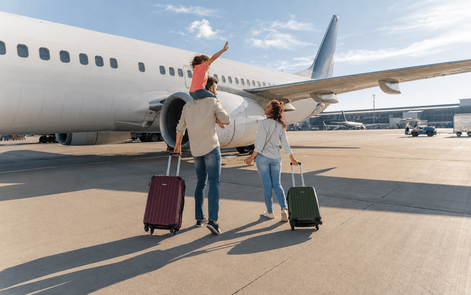Família com uma criança caminha com malas ao lado de um avião no aeroporto.