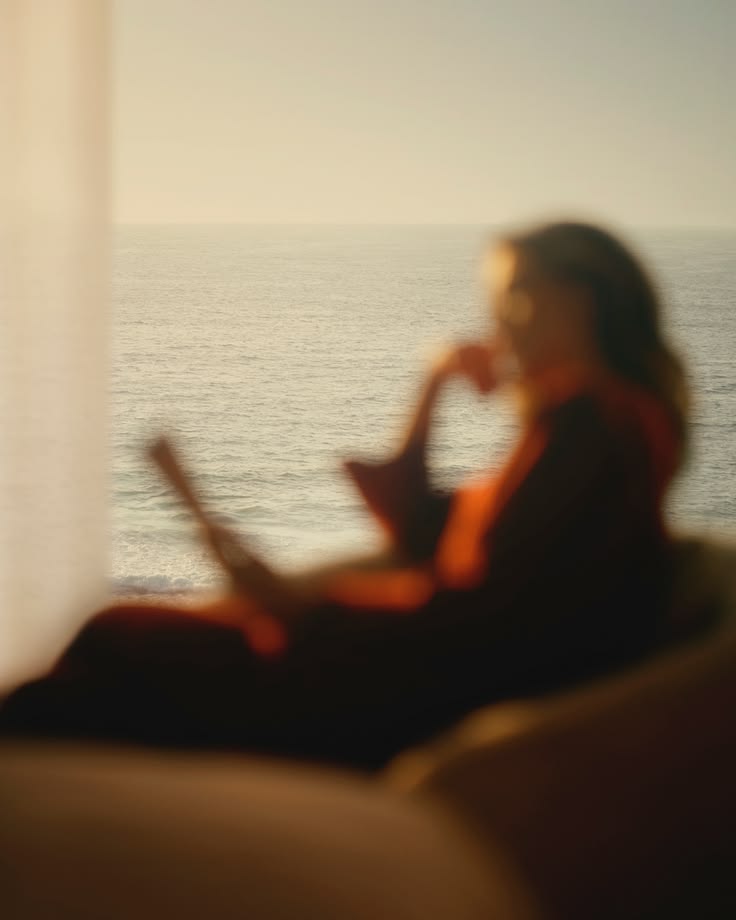 Mulher relaxando com um livro e o mar ao fundo.