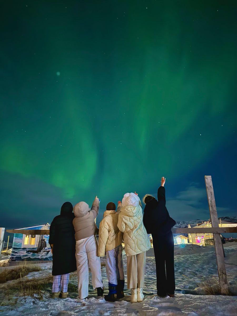 Grupo reunido observando a aurora boreal em uma paisagem nevada.